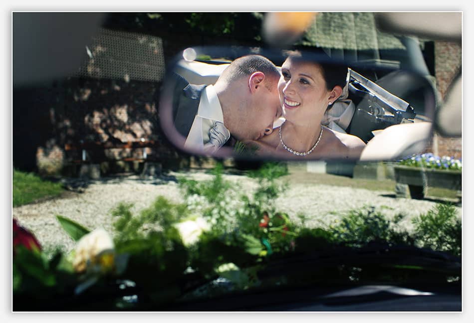 Bruidspaar in de spiegel van hun trouwauto 