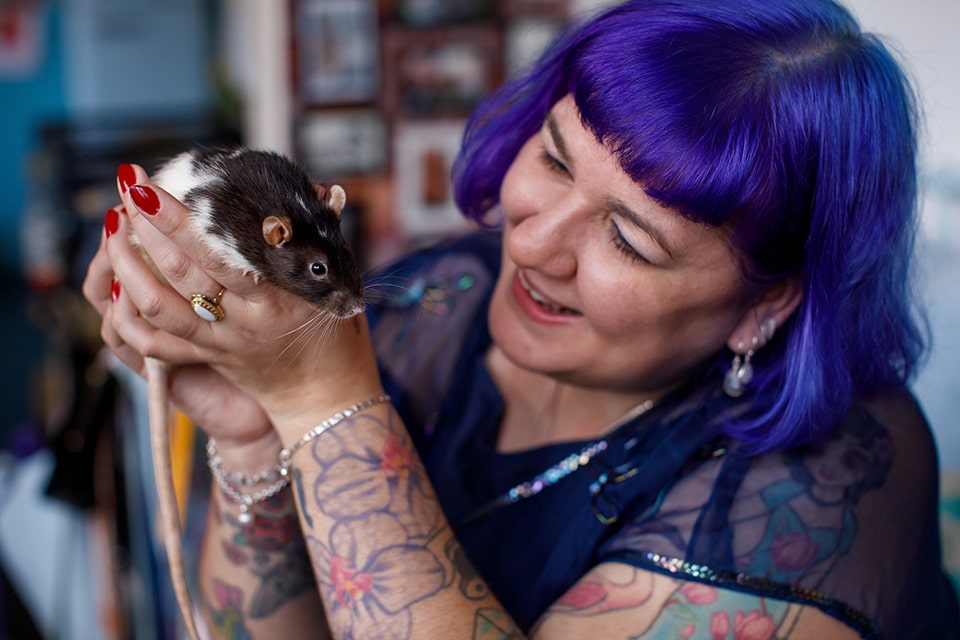 Vrouw met paars haar en tattoos lacht naar het ratje in haar handen