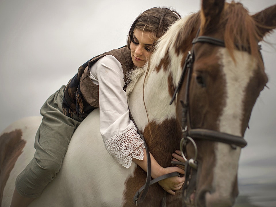 Meisje ligt op paardenrug en slaat innig haar armen om de hals van het dier