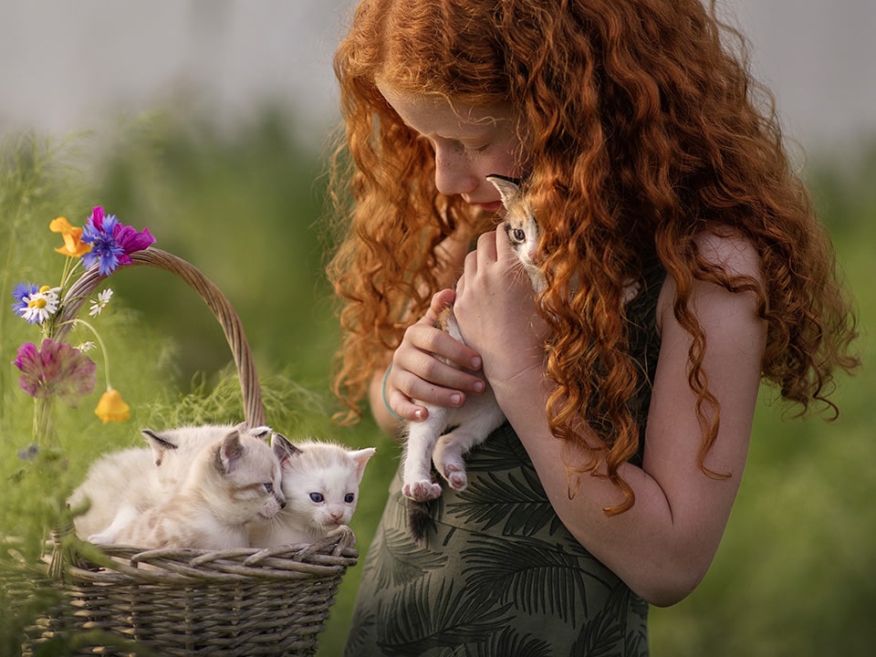 Meisje met rode krullen heeft een mandje met kittens voor zich en knuffelt eentje ervan liefdevol
