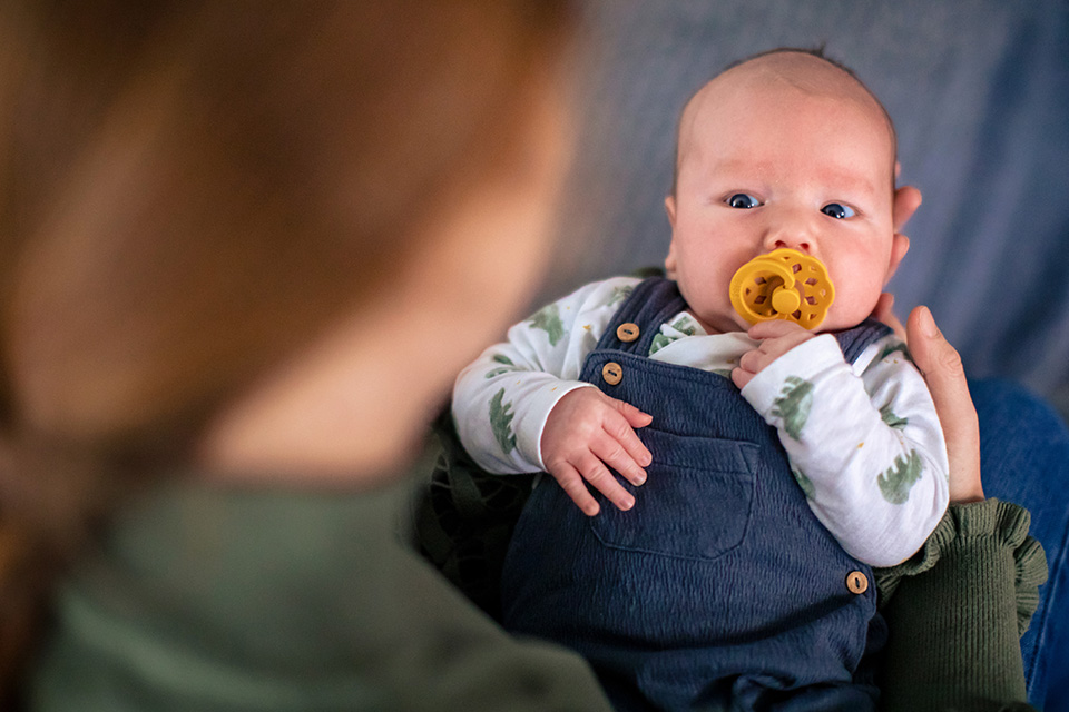 Baby jongen kijkt nieuwsgiering naar zijn moeder terwijl hij op haar schoot ligt