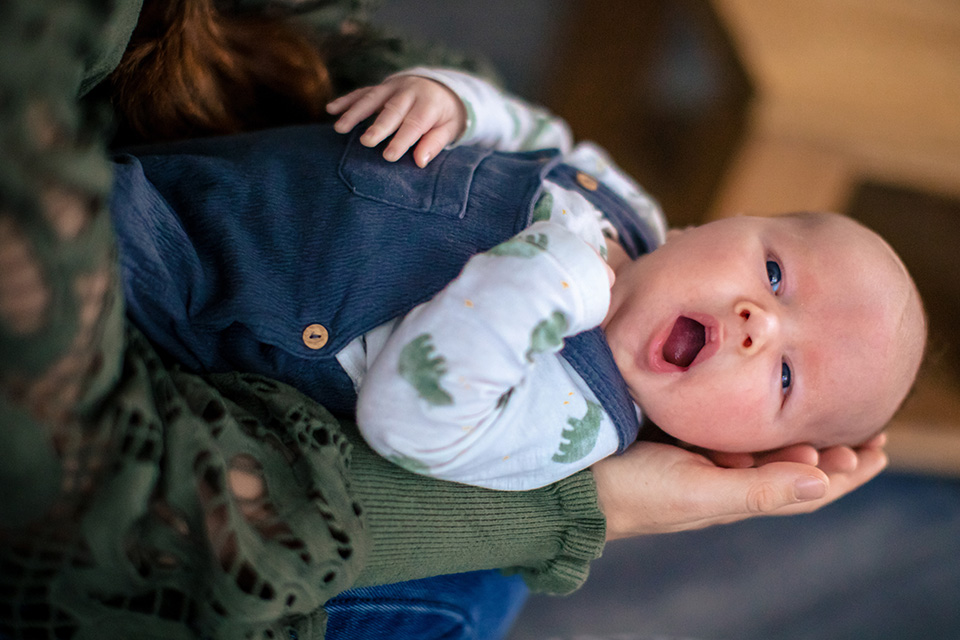 Baby ligt in moeders armen te gapen.