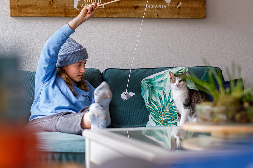 Jonge vrouw zit tijdens thuisreportage op haar bank met kat te spelen