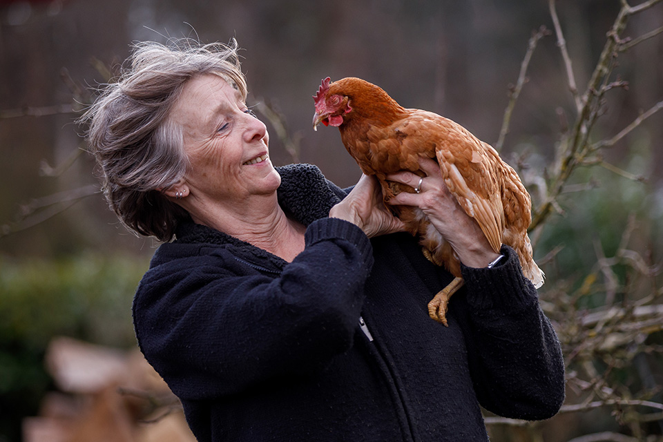 Vrouw kijkt naar kip op haar arm, die genietend haar ogen sluit. 