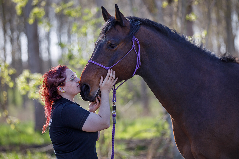 Vrouw met rood haard geeft haar bruine paard in het bos een zachte kus op zijn neus.