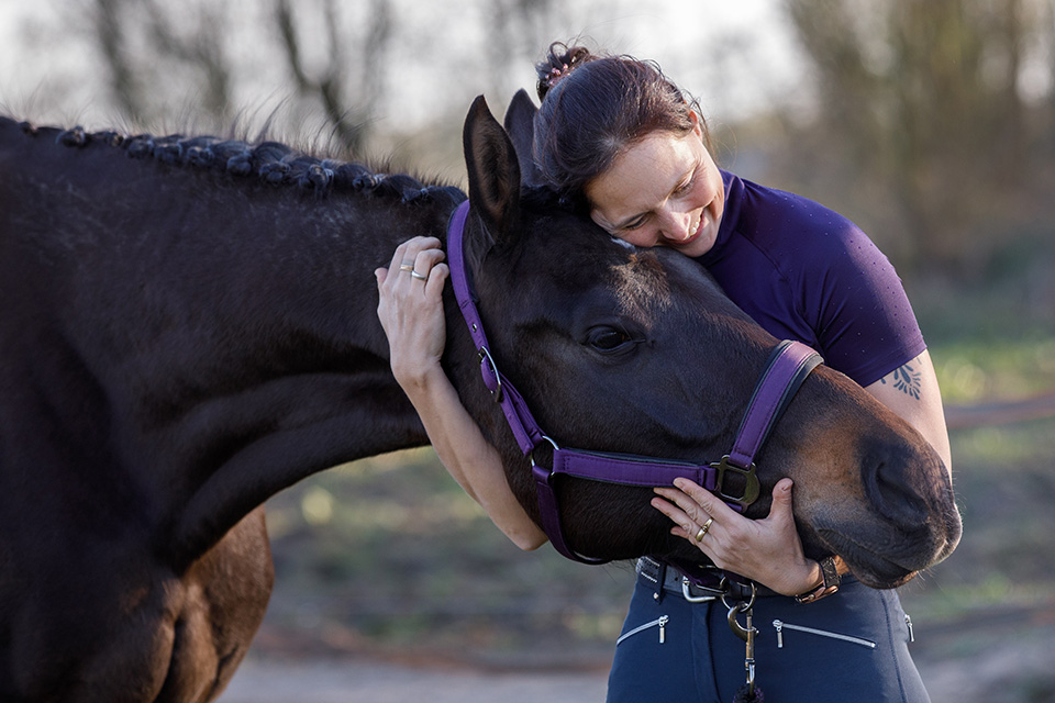Vrouw houdt liefdevol het hoofd van haar paard in haar armen.
