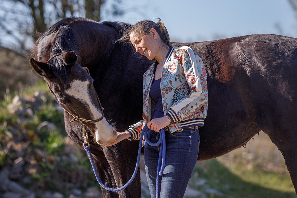 Vrouw leunt met hoofd tegen rug van haar paard terwijl deze zijn hoofd naar haar toebuigt