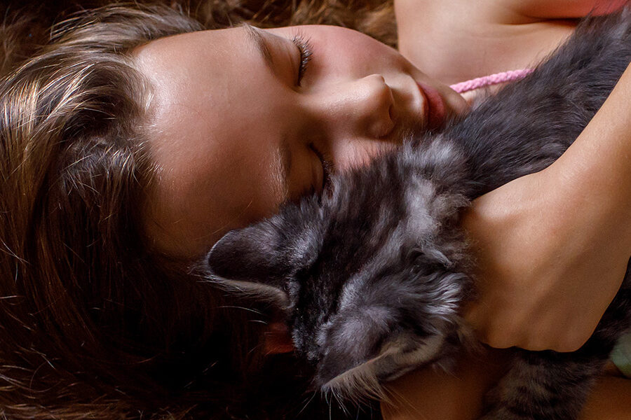 Meisje met heel lang haar ligt liefdevol te knuffelen met een kitten in haar arm